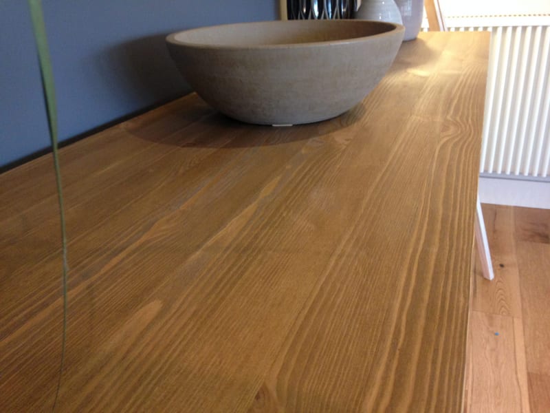 Close-up of the natural wood top of the sideboard, showing the straight grain and waxed finish beside a large stone bowl, with a white radiator and oak floorboards behind