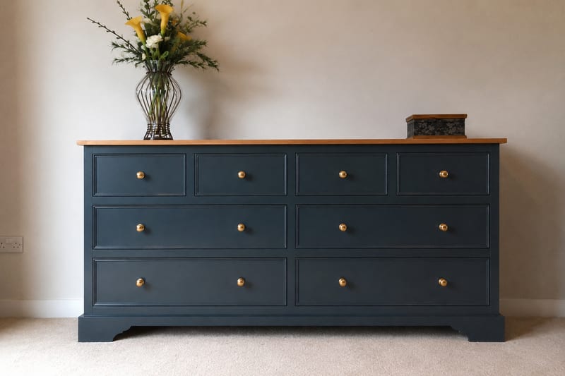 Dark navy painted 6ft sideboard with a solid oak top and eight drawers with brass knobs, standing on a shaped plinth with a vase of flowers on top