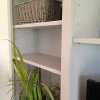 Close view of an outer shelved bay showing a grey wicker basket, adjustable shelves with metal pins, the painted tongue-and-groove back boards and a spider plant in the foreground