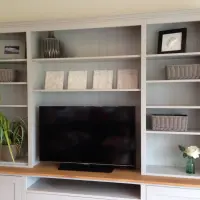 Front view of the upper bookcase section showing three bays of adjustable shelves, wicker baskets, framed prints, a ribbed vase, four small canvases and a television on the oak top