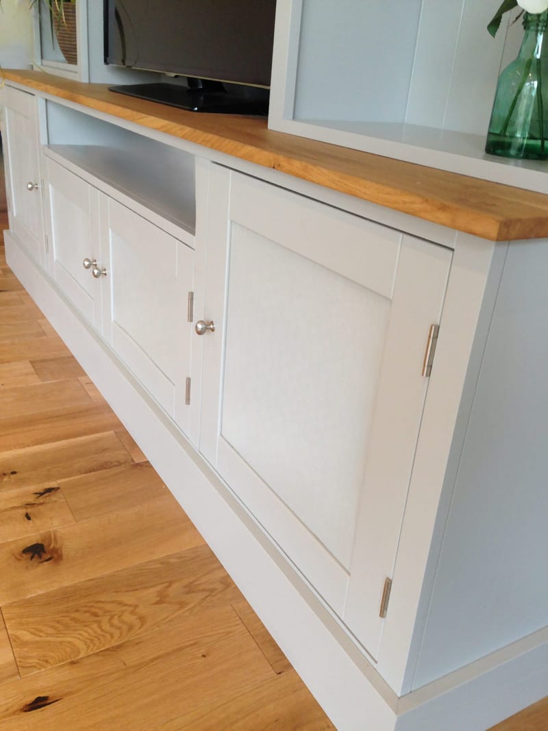 Low angled view of the cupboard base showing the shaker doors with chrome knobs and hinges, the oak worktop overhang, the open television recess and the plinth on oak floorboards