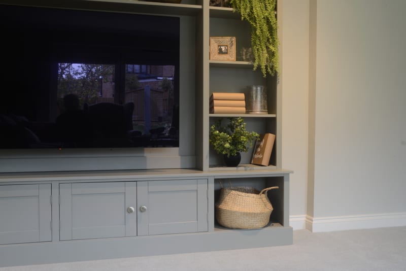 Close view of the right end of the unit, with shelves holding a framed photograph, trailing artificial plant, stacked books and a plant in a black pot above a woven basket in the base cubby