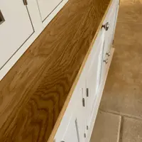 Close view along the oiled oak worktop of the cream dresser, showing the golden grain, square front edge and the row of round brushed nickel knobs on the drawers and doors below