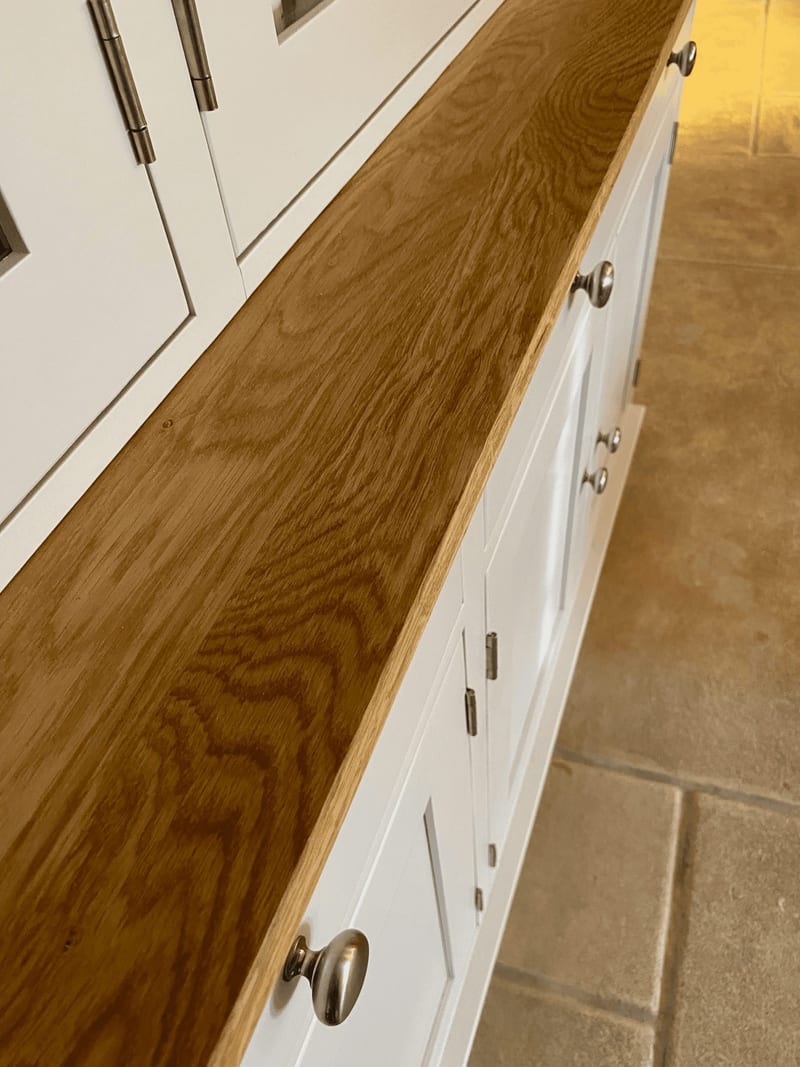 Close view along the oiled oak worktop of the cream dresser, showing the golden grain, square front edge and the row of round brushed nickel knobs on the drawers and doors below