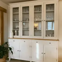 Angled view showing the depth of the dresser, with the moulded cornice, four glazed doors, oak worktop, two drawers and four shaker cupboards above turned bun feet on a flagstone floor