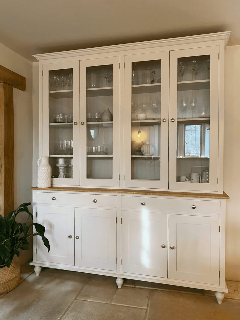 Angled view showing the depth of the dresser, with the moulded cornice, four glazed doors, oak worktop, two drawers and four shaker cupboards above turned bun feet on a flagstone floor