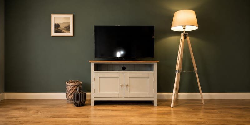 Cream painted 3ft shaker style TV cabinet with a solid oak top, an open media shelf and two cupboard doors, with a television on top against a deep green wall