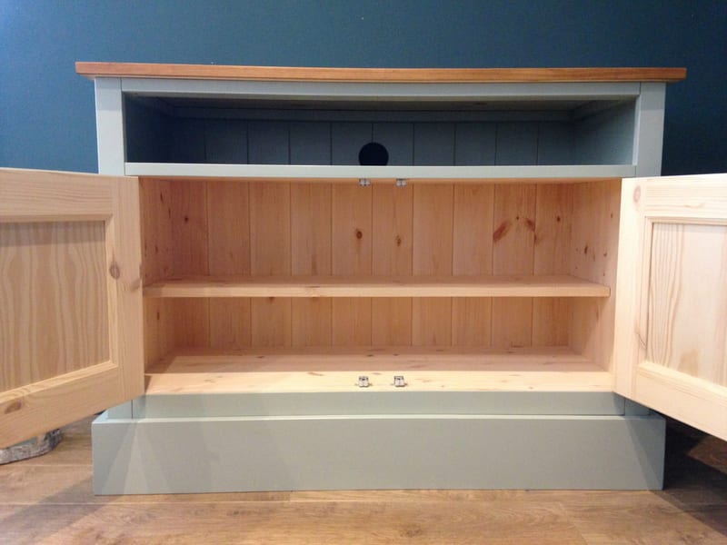 Front view with both cupboard doors open, showing the bare pine interior and fixed shelf, the painted open shelf above with a round cable hole, and the pine doors seen from the inside