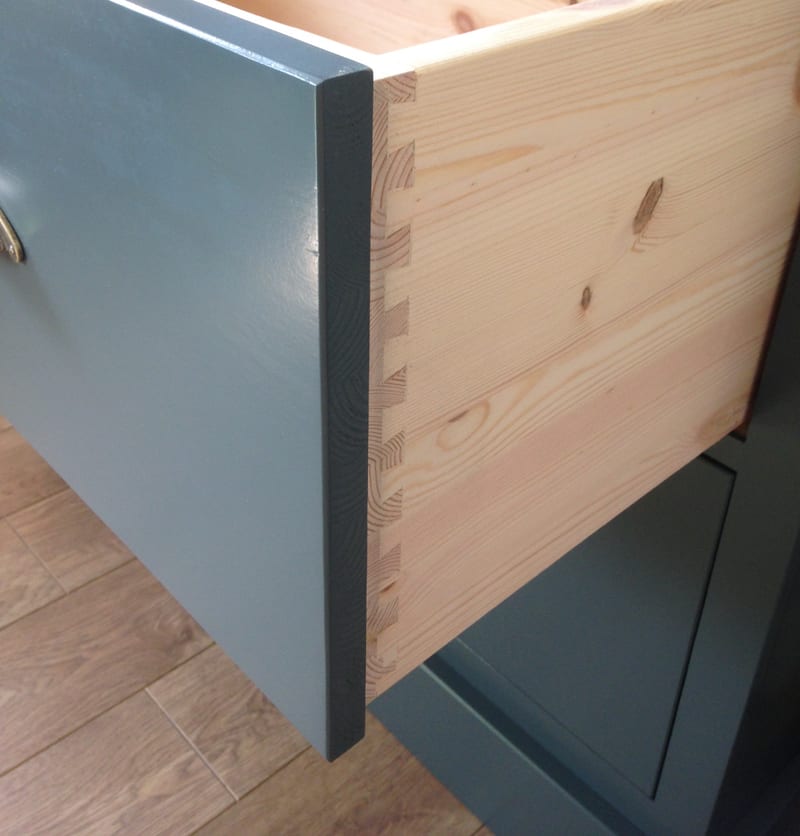 Detail of a drawer pulled out of the teal painted dresser base, showing the hand-cut dovetail joints and the knotty natural pine drawer box behind the painted front