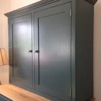 Angled view of the upper cabinet from the right, showing the depth of the teal painted side panel, brushed nickel hinges, brass knobs and the oak worktop and drawer front beneath