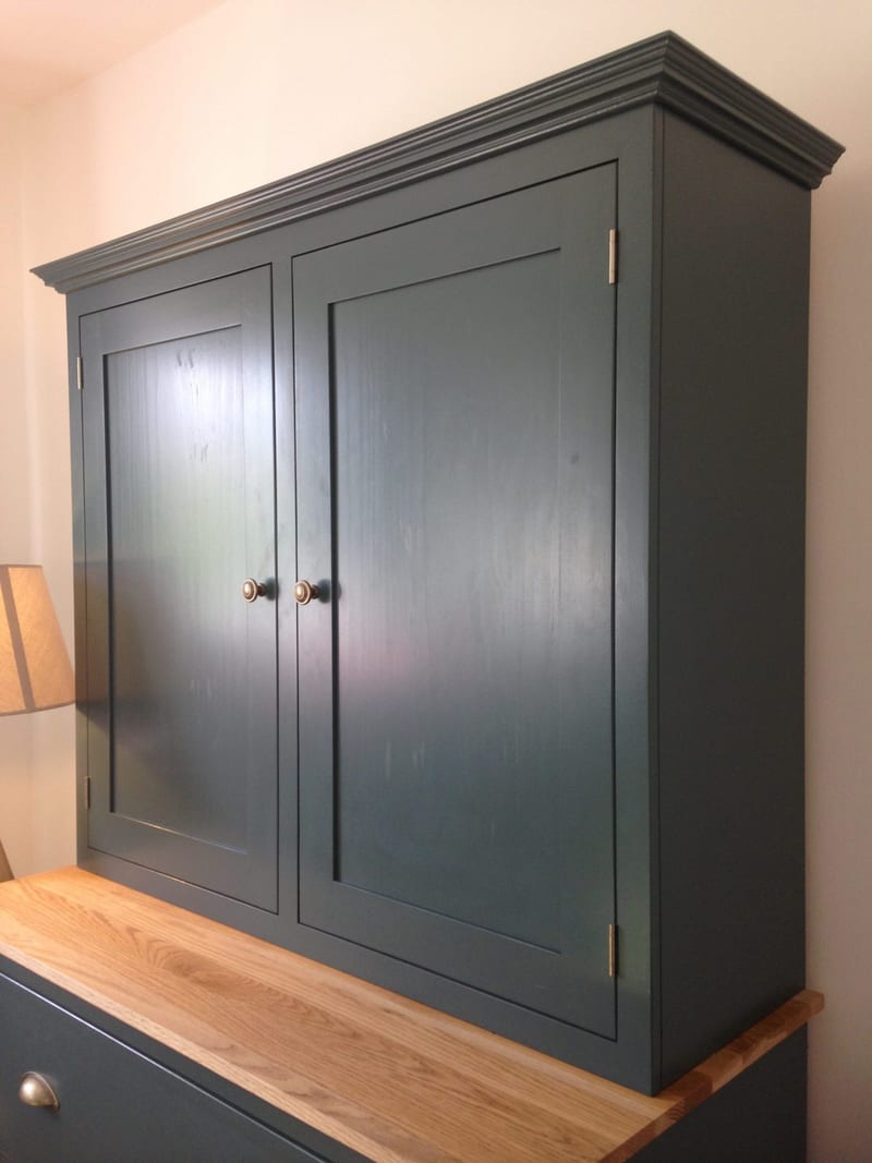 Angled view of the upper cabinet from the right, showing the depth of the teal painted side panel, brushed nickel hinges, brass knobs and the oak worktop and drawer front beneath