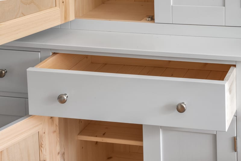 Close view of an open drawer, showing the light grey painted front with two brushed nickel knobs and the natural pine base and sides of the drawer box, above an open pine-lined cupboard