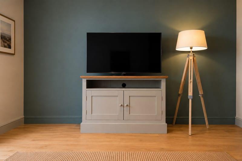 Compact grey painted 3ft TV media base unit with a solid oak top, an open media shelf with a cable hole and two shaker doors below, with a television on top against a dark green wall