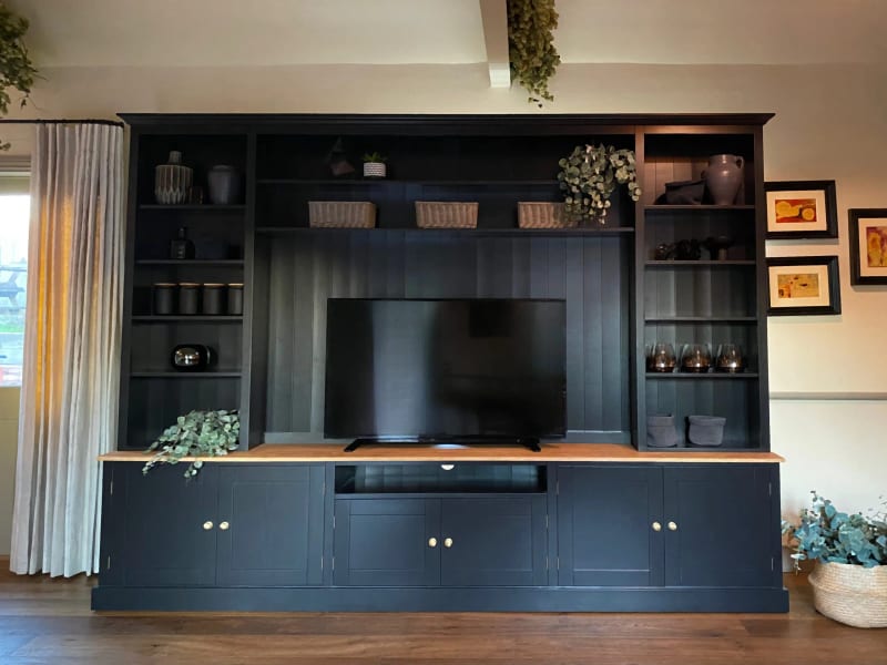 Straight-on view of the navy painted media unit, showing the symmetrical open shelving either side of the television, the oak worktop and the panelled cupboards below on a wood floor