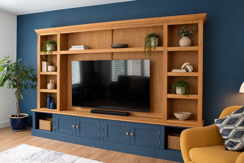 Front view of the 10ft Woburn media unit against a navy wall, with a navy painted cupboard base, oak open shelving either side of a large television and an oak veneer backboard