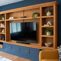 Angled view of the Woburn media unit showing the oak top section with open shelves styled with plants, books and ceramics above navy painted cupboards with brass knobs