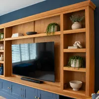 Angled view from the left of the oak media unit, a potted tree beside the left-hand shelving and a soundbar on the worktop beneath the television