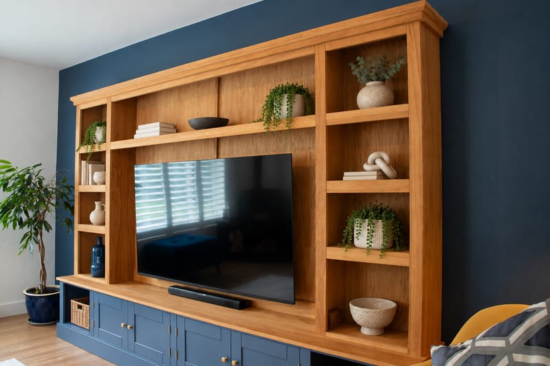 Angled view from the left of the oak media unit, a potted tree beside the left-hand shelving and a soundbar on the worktop beneath the television