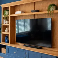 Close view of the left-hand side of the unit, showing the oak shelves with blue glass vases, a stoneware jug and trailing plants beside the television recess