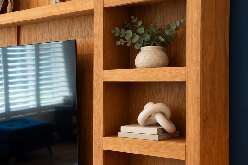 Close-up of the oak shelving joinery and grain, with a eucalyptus stem in a stoneware vase and a ceramic knot ornament resting on books