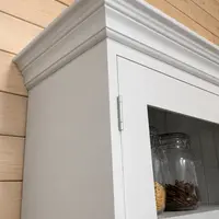 Corner detail of the moulded cornice on the painted dresser top, showing the layered mouldings, the door hinge and glass panel with a jar of dried sticks on the shelf behind