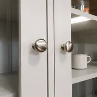 Close-up of two brushed nickel round knobs on the meeting stiles of the glazed dresser doors, with a speckled cream mug and grey painted shelves visible through the glass behind