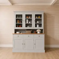 Wide room view of the grey dresser standing against a pale timber clad wall, showing the glazed top, oak worktop and plinth base on a light wood floor in an empty styled room