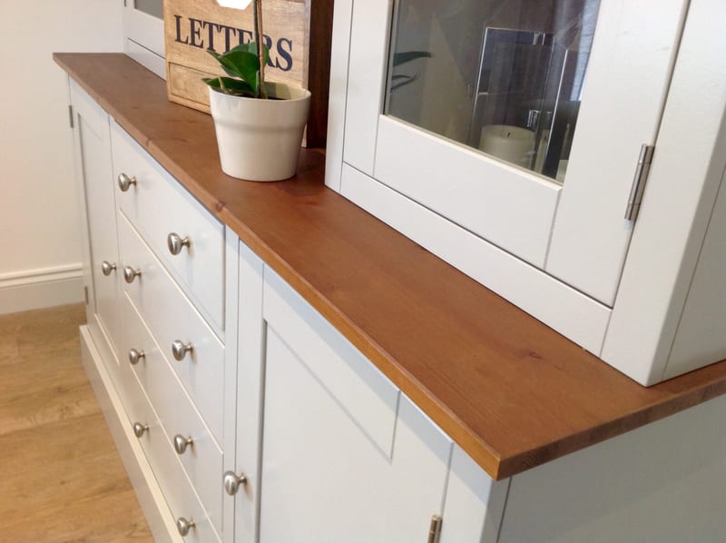 Angled view along the warm pine top of the dresser base, showing a bank of drawers with brushed nickel knobs, a cupboard door and the glazed upper doors with a potted plant on the top