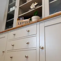 Low angled view of the four central drawers and flanking cupboard doors, all with brushed nickel knobs, below the pine top holding a wooden letters box and a white orchid