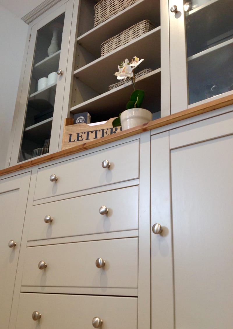 Low angled view of the four central drawers and flanking cupboard doors, all with brushed nickel knobs, below the pine top holding a wooden letters box and a white orchid