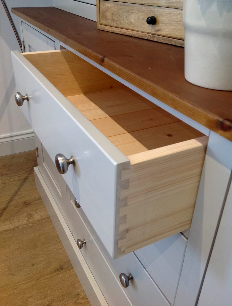 Detail of a drawer pulled fully out of the painted base, showing the hand-cut dovetail joints and solid pine drawer box behind a painted front with a brushed nickel knob