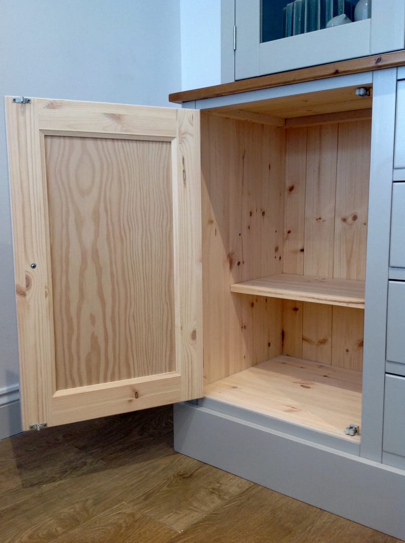 Base cupboard with the door open, showing the bare pine reverse of the panelled door and the natural pine carcass inside with a fixed shelf above the painted plinth