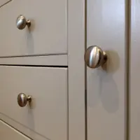 Close-up of three brushed nickel knobs on the painted drawer and door fronts, showing the rounded knob profile and the shadow gaps between each drawer front