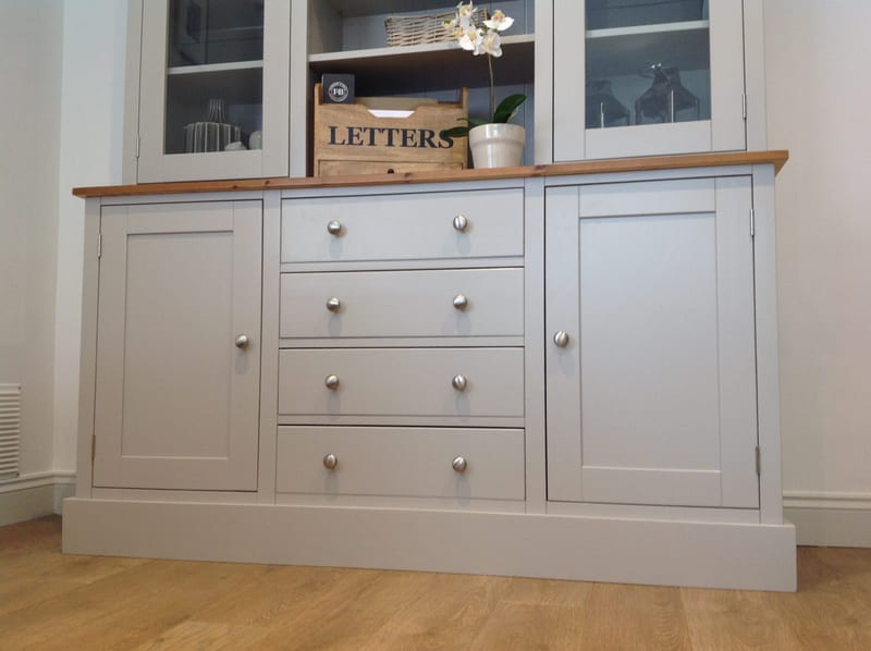 Front view of the dresser base, showing a cupboard door each side of four equal drawers with paired brushed nickel knobs, a pine top and a stepped plinth on a wooden floor