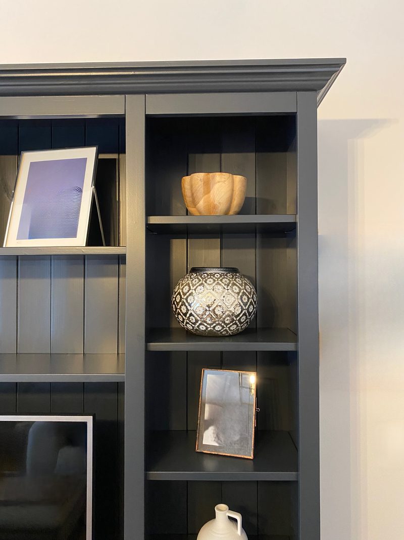 Angled view of the right bookcase column, showing the moulded cornice, three shelves with a turned wooden bowl, a patterned ceramic lantern and a copper framed picture against the panelled back