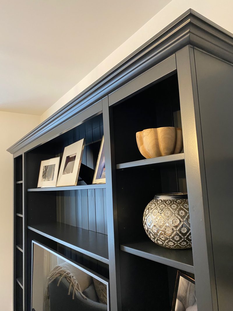 Upward angled view of the top of the media unit, showing the moulded cornice, three framed prints on the central shelf and a wooden bowl and patterned lantern in the side column