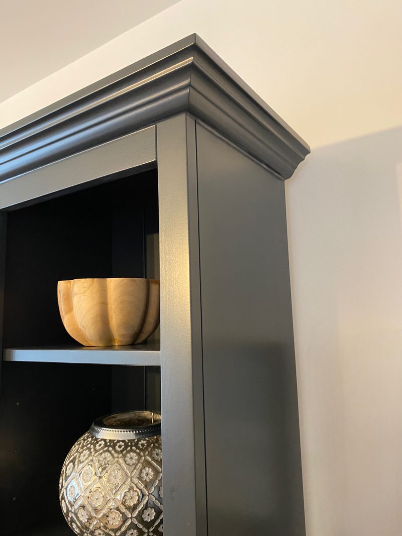 Corner detail of the moulded cornice on the dark painted media unit, showing the mitred return, the flat painted end panel and a turned wooden bowl on the shelf inside