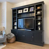 Angled room view of the full media unit against a cream wall, with a grey sofa, wicker basket and carved wall panel alongside it and a curtained window on the left