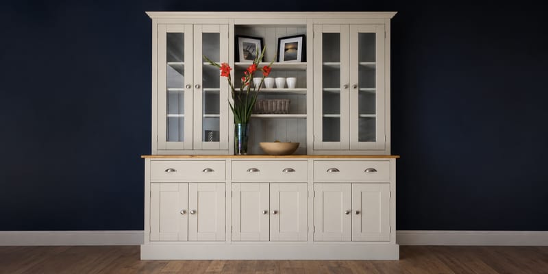 Grey painted 6ft Radwell Welsh dresser with glazed doors either side of an open plate shelf, above three cup handled drawers and six cupboard doors, against a deep navy wall