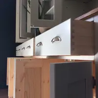 Low angle along the open base, showing a natural pine drawer box with hand-cut dovetail joints, cup handles on the painted fronts and cupboard doors swung open to reveal bare pine backs