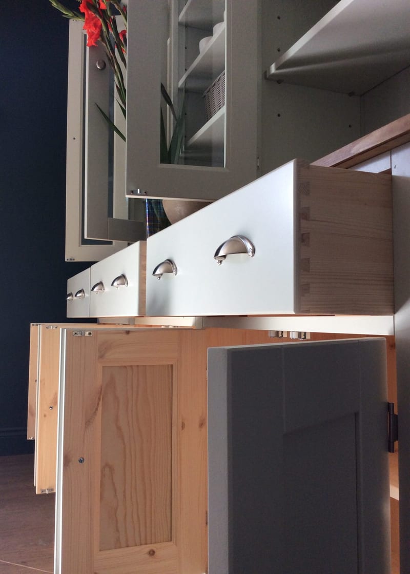 Low angle along the open base, showing a natural pine drawer box with hand-cut dovetail joints, cup handles on the painted fronts and cupboard doors swung open to reveal bare pine backs