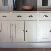 Straight-on view of the base cabinet, showing three drawers with brushed nickel cup handles, six panelled doors with round knobs, a stone bowl on the oiled timber top and the plinth on a wood floor