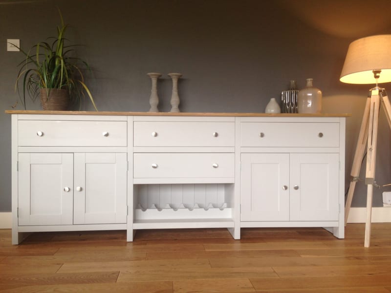 Straight-on front view of the white sideboard, showing three top drawers, a fourth drawer over the slatted wine rack, two pairs of panelled doors and grey candlesticks against a charcoal wall