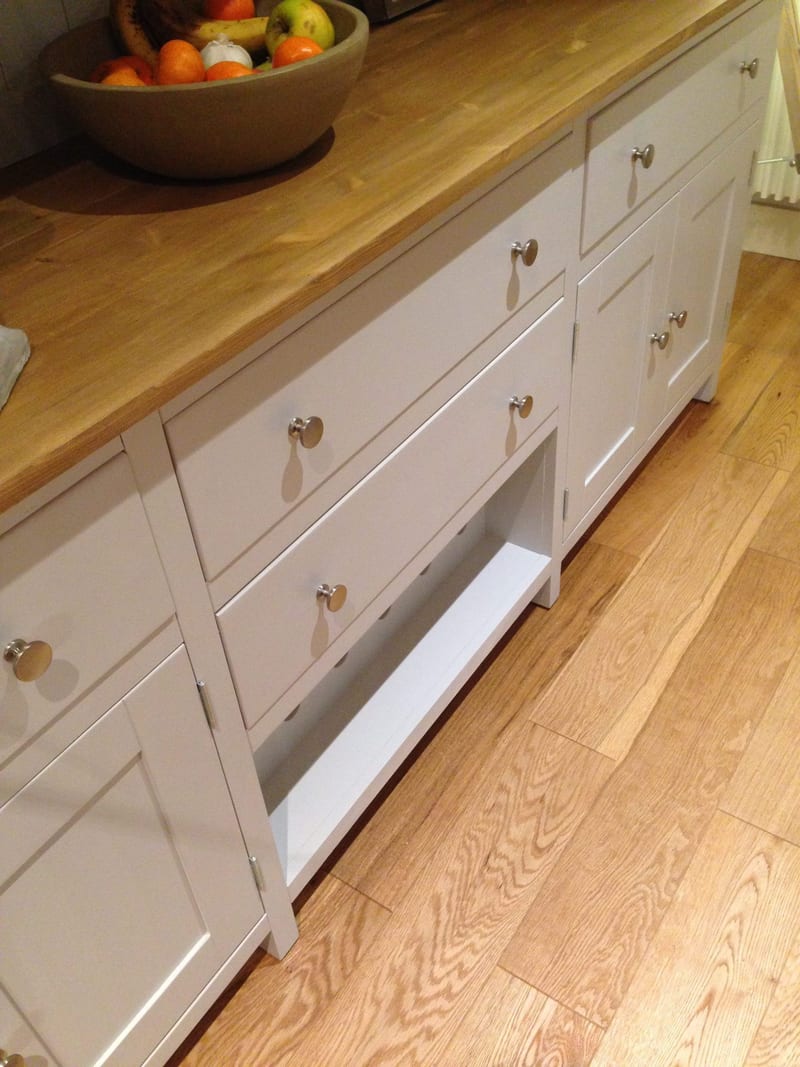 Close angled view down onto the base, showing the oiled timber top with a stoneware bowl of fruit, drawers with round brushed nickel knobs and the open wine rack shelf above an oak floor