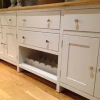 Low view of the base from the left, showing three top drawers with round brushed nickel knobs, panelled cupboard doors and a fourth drawer above the wine rack in the centre bay