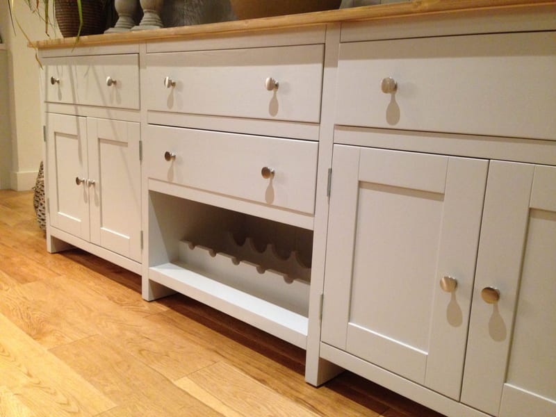 Low view of the base from the left, showing three top drawers with round brushed nickel knobs, panelled cupboard doors and a fourth drawer above the wine rack in the centre bay