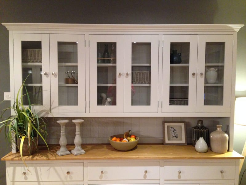 Front view of the glazed upper section, showing six glazed doors, shelves of wicker baskets, bottles and a white jug, with candlesticks, a bowl of fruit and a framed bird print below