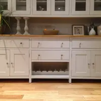 Front view of the base with the glazed top cropped above, showing three top drawers, a fourth over the centre wine rack, four panelled doors and candlesticks and a fruit bowl on the timber top