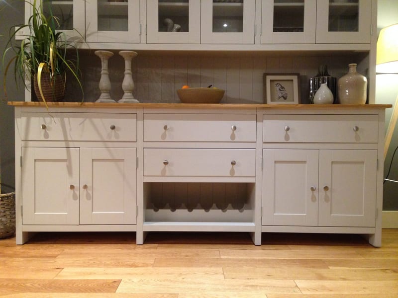 Front view of the base with the glazed top cropped above, showing three top drawers, a fourth over the centre wine rack, four panelled doors and candlesticks and a fruit bowl on the timber top
