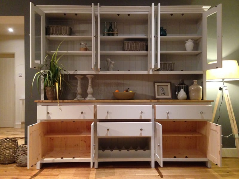 Front view with all doors open, showing tongue-and-groove backed shelves holding baskets and bottles above, bare pine cupboard interiors below and the centre drawer pulled out